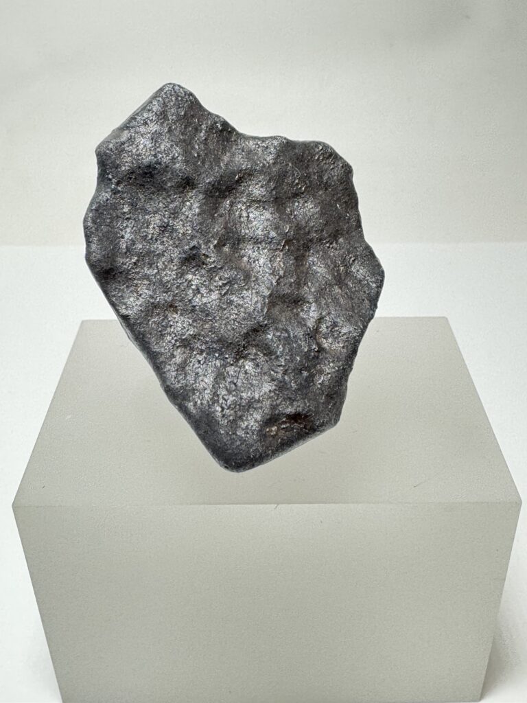 Dark, irregularly shaped McDonough meteorite specimen on a light-colored display pedestal.
